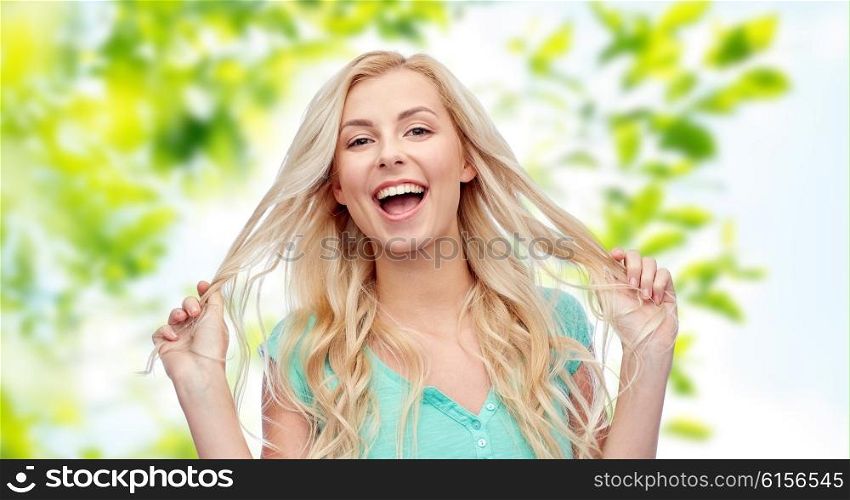 emotions, expressions, hairstyle and people concept - smiling young woman or teenage girl holding her strand of hair over green natural background