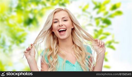 emotions, expressions, hairstyle and people concept - smiling young woman or teenage girl holding her strand of hair over green natural background