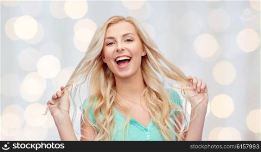 emotions, expressions, hairstyle and people concept - smiling young woman or teenage girl holding her strand of hair over holidays lights background