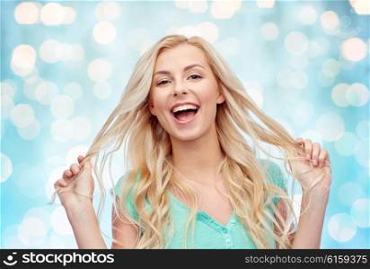 emotions, expressions, hairstyle and people concept - smiling young woman or teenage girl holding her strand of hair over blue holidays lights background