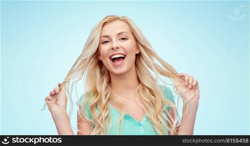 emotions, expressions, hairstyle and people concept - smiling young woman or teenage girl holding her strand of hair over blue background