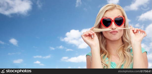 emotions, expressions, hairstyle and people concept - smiling young woman or teenage girl making mustache with strand of hair over blue sky and clouds background