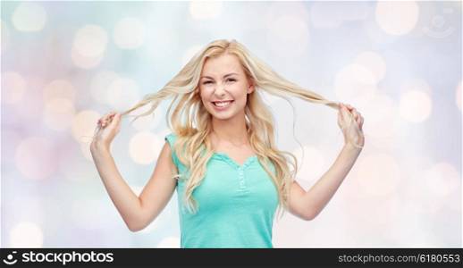 emotions, expressions, hairstyle and people concept - smiling young woman or teenage girl holding strands of her hair over holidays lights background
