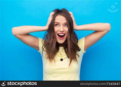 emotions, expressions, hairstyle and people concept - smiling young woman or teenage girl holding to her head or touching hair over bright blue background. smiling young woman holding to her head