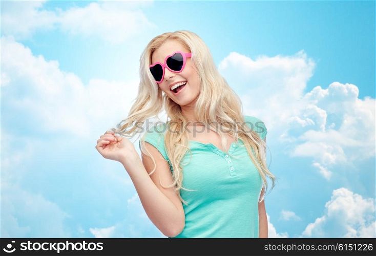 emotions, expressions, summer and people concept - smiling young woman or teenage girl in sunglasses holding her strand of hair over blue sky and clouds background