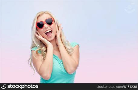 emotions, expressions, summer and people concept - smiling young woman or teenage girl in heart shape sunglasses over pink background