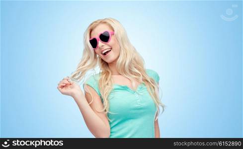 emotions, expressions, summer and people concept - smiling young woman or teenage girl in sunglasses holding her strand of hair over blue background
