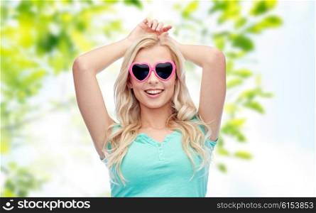 emotions, expressions, summer and people concept - smiling young woman or teenage girl in heart shape sunglasses over green natural background