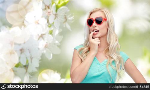 emotions, expressions, summer and people concept - smiling young woman or teenage girl in sunglasses over natural spring cherry blossom background