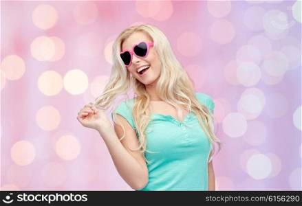 emotions, expressions, summer and people concept - smiling young woman or teenage girl in sunglasses holding her strand of hair over pink holidays lights background