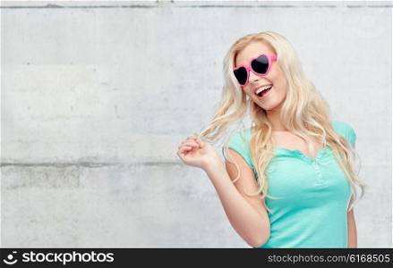 emotions, expressions, summer and people concept - smiling young woman or teenage girl in sunglasses holding her strand of hair over gray concrete wall background