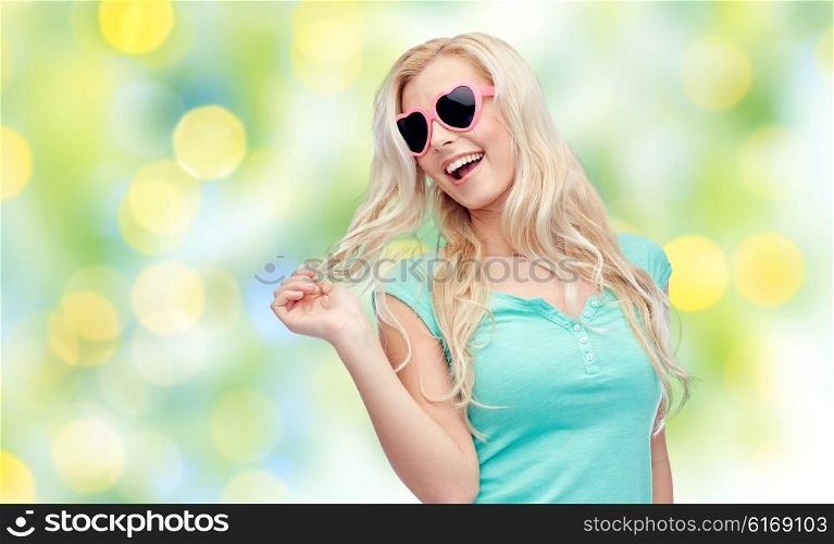 emotions, expressions, summer and people concept - smiling young woman or teenage girl in sunglasses holding her strand of hair over summer green lights background