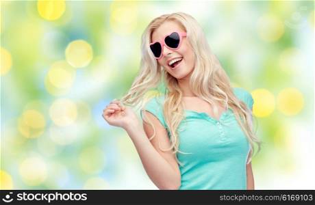 emotions, expressions, summer and people concept - smiling young woman or teenage girl in sunglasses holding her strand of hair over summer green lights background