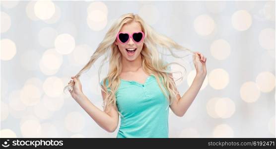 emotions, expressions, summer and people concept - smiling young woman or teenage girl in sunglasses holding her strand of hair over holidays lights background