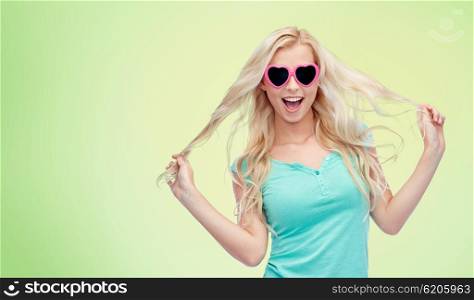 emotions, expressions, summer and people concept - smiling young woman or teenage girl in sunglasses holding her strand of hair over green natural background