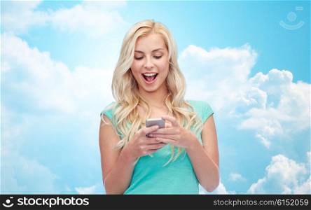 emotions, expressions, technology and people concept - smiling young woman or teenage girl texting on smartphone over blue sky and clouds background