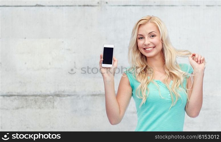 emotions, expressions, technology and people concept - smiling young woman or teenage girl showing blank smartphone screen over gray concrete wall background