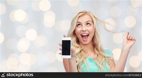 emotions, expressions, technology and people concept - smiling young woman or teenage girl showing blank smartphone screen over holidays lights background