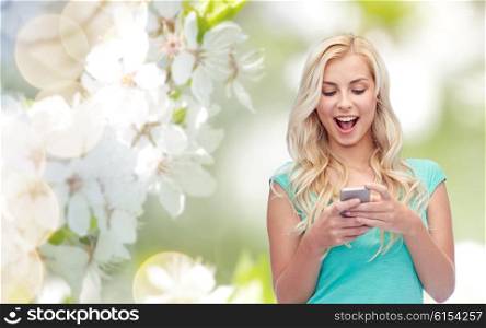 emotions, expressions, technology and people concept - smiling young woman or teenage girl texting on smartphone over natural spring cherry blossom background