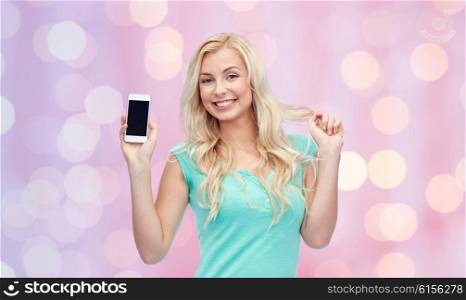 emotions, expressions, technology and people concept - smiling young woman or teenage girl showing blank smartphone screen over pink holidays lights background