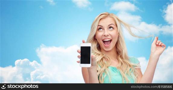 emotions, expressions, technology and people concept - smiling young woman or teenage girl showing blank smartphone screen over blue sky and clouds background