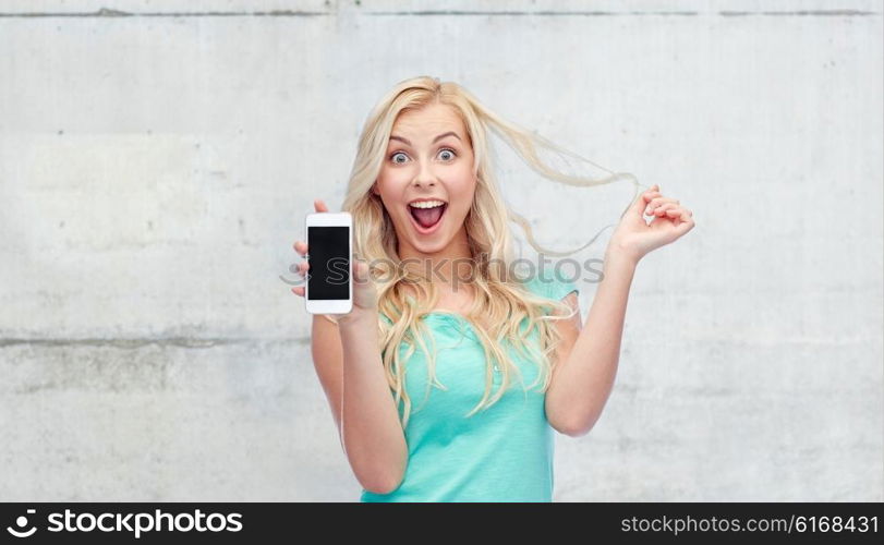 emotions, expressions, technology and people concept - smiling young woman or teenage girl showing blank smartphone screen over gray concrete wall background