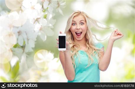 emotions, expressions, technology and people concept - smiling young woman or teenage girl showing blank smartphone screen over natural spring cherry blossom background