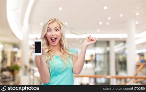 emotions, expressions, technology and people concept - smiling young woman or teenage girl showing blank smartphone screen over mall or shopping center background