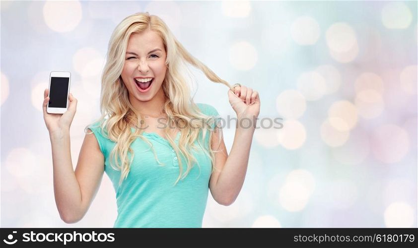 emotions, expressions, technology and people concept - smiling young woman or teenage girl showing blank smartphone screen and winking over holidays lights background