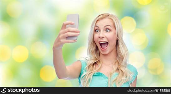 emotions, expressions, technology, summer and people concept - happy smiling young woman or teenage girl taking selfie with smartphone over green lights background