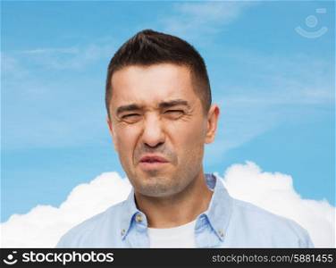 emotions, facial expression and people concept - man wrying of unpleasant smell over blue sky and cloud background