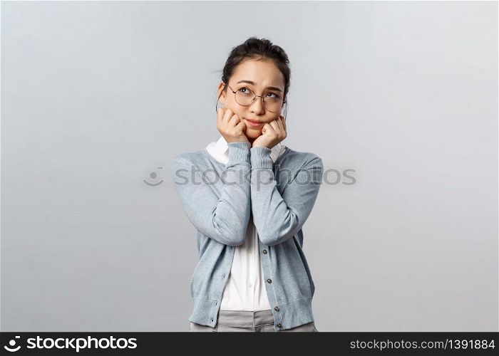 Emotions, people and lifestyle concept. Adorable dreamy and romantic asian girl in glasses, sighing daydreaming, being in love, thinking about dating guy she likes, standing grey background.. Emotions, people and lifestyle concept. Adorable dreamy and romantic asian girl in glasses, sighing daydreaming, being in love, thinking about dating guy she likes, standing grey background