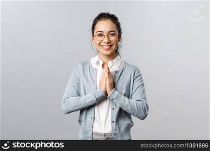 Emotions, people and lifestyle concept. Friendly cute asian woman in glasses, hold hands in pray or namaste gesture, smiling cheerful, greeting person politely, standing grey background.. Emotions, people and lifestyle concept. Friendly cute asian woman in glasses, hold hands in pray or namaste gesture, smiling cheerful, greeting person politely, standing grey background