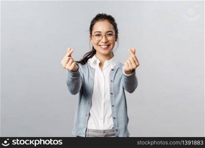 Emotions, people and lifestyle concept. Optimistic good-looking asian female in glasses, showing korean hearts gesture with fingers and smiling, express love sympathy and admiration.. Emotions, people and lifestyle concept. Optimistic good-looking asian female in glasses, showing korean hearts gesture with fingers and smiling, express love sympathy and admiration