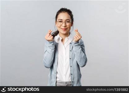 Emotions, people and lifestyle concept. Optimistic, lovely and cute asian girl in glasses express sympathy or joy, showing korean heart signs with fingers, looking kawaii, standing grey background.. Emotions, people and lifestyle concept. Optimistic, lovely and cute asian girl in glasses express sympathy or joy, showing korean heart signs with fingers, looking kawaii, standing grey background