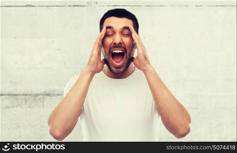 emotions, stress, madness and people concept - crazy shouting man in t-shirt over gray wall background. crazy shouting man in t-shirt over gray wall