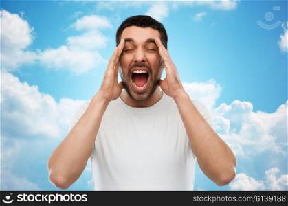 emotions, stress, madness and people concept - crazy shouting man in t-shirt over blue sky and clouds background