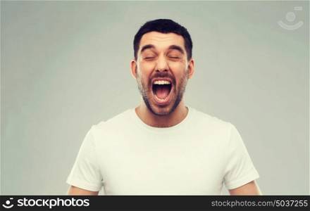 emotions, stress, madness and people concept - crazy shouting man in t-shirt over gray background. crazy shouting man in t-shirt over gray background