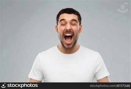 emotions, stress, madness and people concept - crazy shouting man in t-shirt over gray background