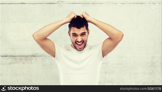 emotions, stress, madness and people concept - crazy shouting man rending ones hair in t-shirt over gray stone wall background. crazy shouting man in t-shirt over gray background