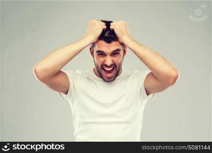 emotions, stress, madness and people concept - crazy shouting man rending ones hair in t-shirt over gray background. crazy shouting man in t-shirt over gray background