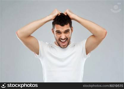 emotions, stress, madness and people concept - crazy shouting man rending ones hair in t-shirt over gray background