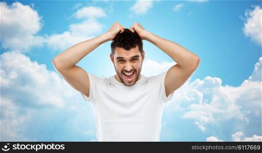 emotions, stress, madness and people concept - crazy shouting man rending ones hair in t-shirt over blue sky and clouds background