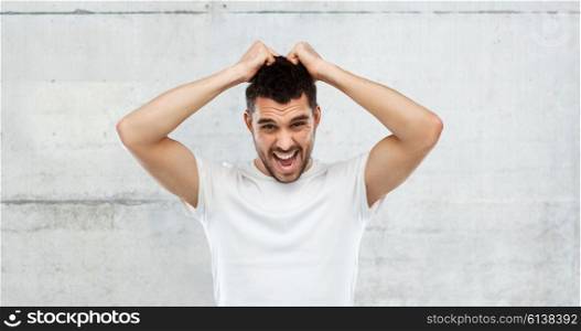 emotions, stress, madness and people concept - crazy shouting man rending ones hair in t-shirt over gray stone wall background