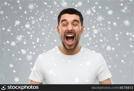 emotions, stress, winter, christmas and people concept - crazy shouting man in t-shirt over snow on gray background