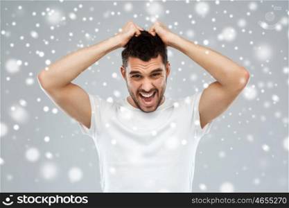 emotions, stress, winter, christmas and people concept - crazy shouting man rending ones hair in t-shirt over snow on gray background