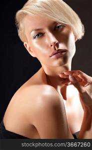 Emotive dark portrait of a blond young woman with an up do and naked shoulder on black background