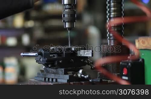Employee cutting hole boring in flat metal piece on drilling machine in workshop.