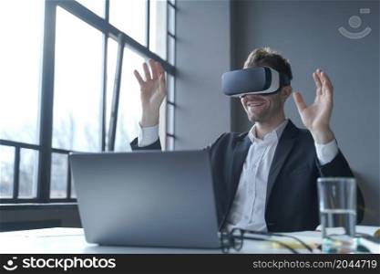 Employee experience with virtual reality. Young businessman in suit sitting at office table and using vr glasses goggles at work, male entrepreneur testing innovative method for business. Young businessman in suit sitting at office table and using vr glasses goggles at work