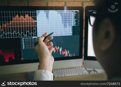 Employees analyze the graph of the stock market using a pen pointing to the computer screen.
